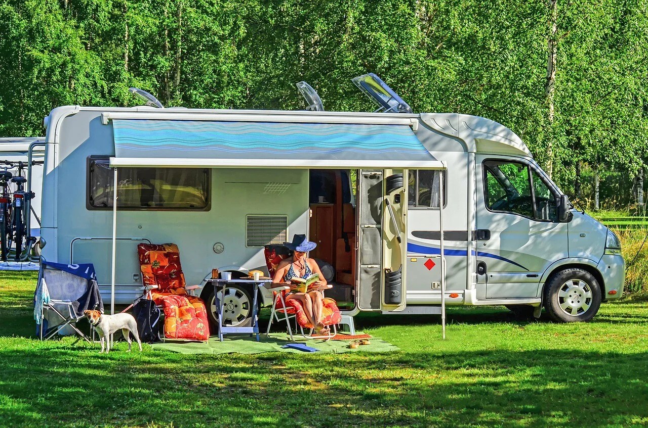RV parked on a grassy campsite with a couple relaxing outside and a dog nearby, symbolizing safe RV travel with pets.
