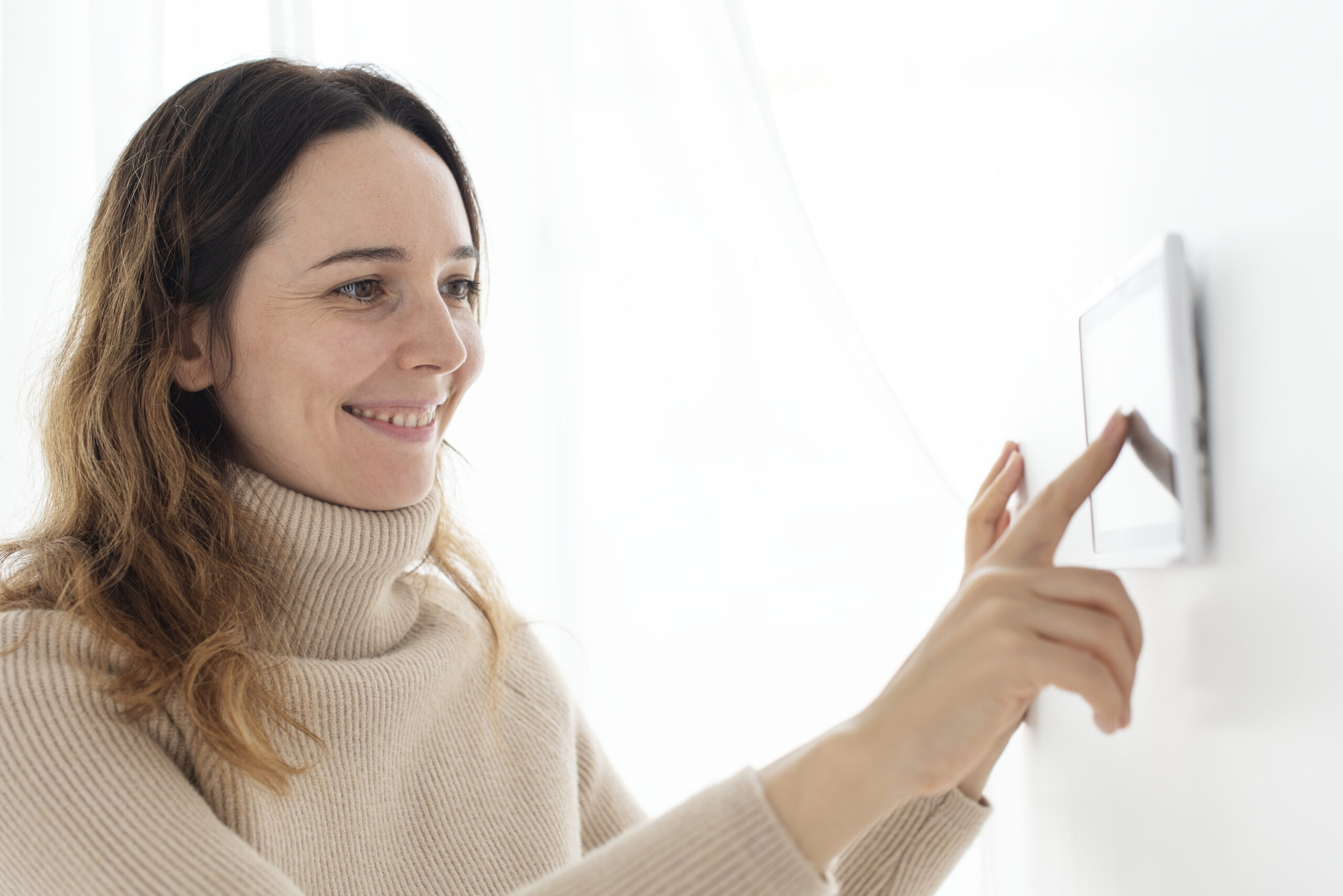 Woman adjusting smart home thermostat to monitor vacation home remotely.