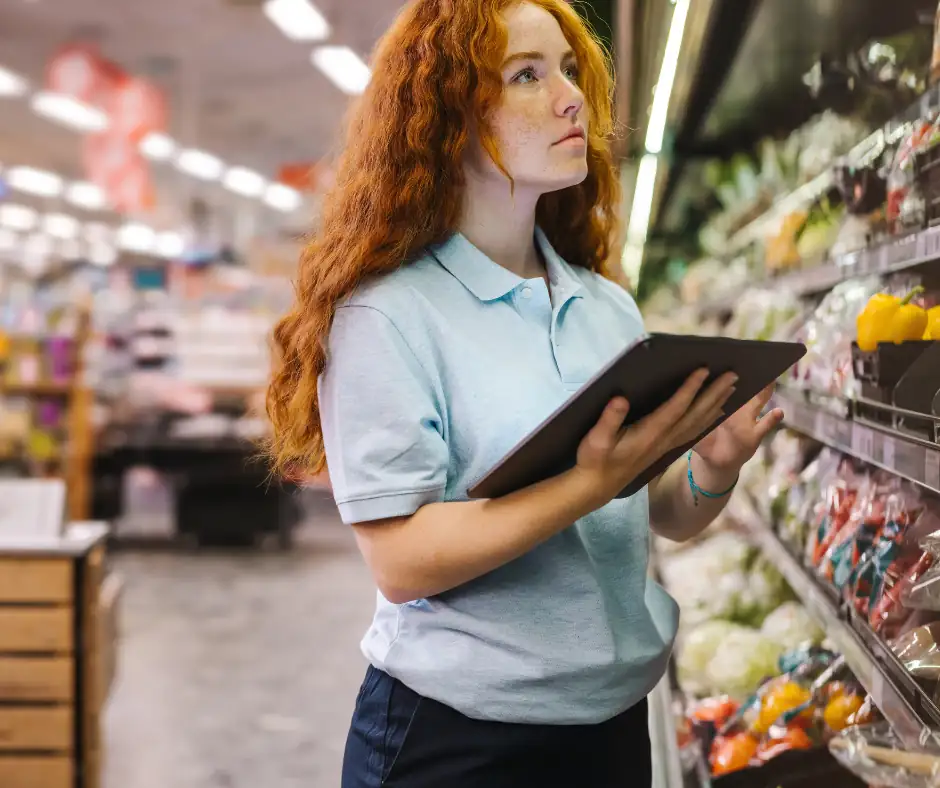 Employee checking produce section with a tablet, representing temperature and food safety monitoring in supermarkets with MarCELL.