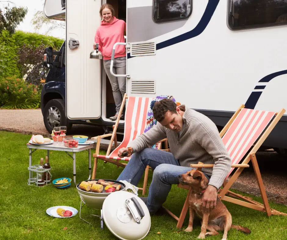 Couple camping beside an RV with a dog and a small barbecue, representing RV and pet monitoring with MarCELL.